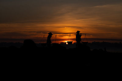 Silhouette people standing on shore against sky during sunset