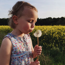 Close-up of girl blowing dandelion while standing at rape farm