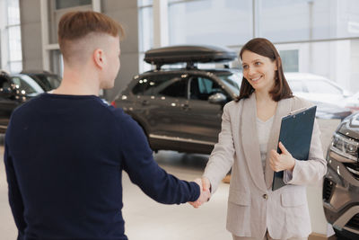 Side view of young woman standing against car