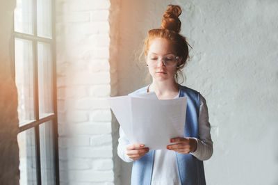 Woman reading documents while sitting against wall