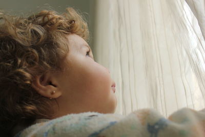 Close-up of cute baby girl looking through curtain on window