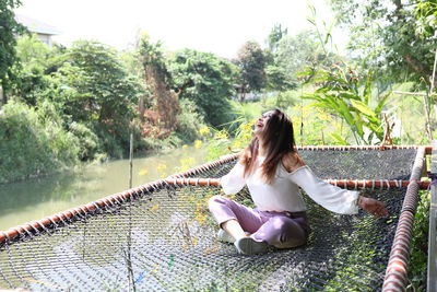 Woman sitting by plants against trees