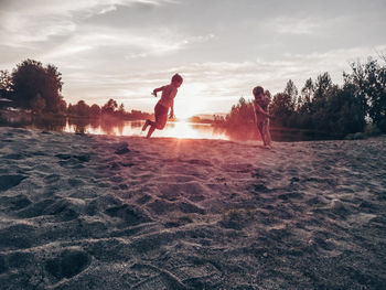 Male friends playing on sand at lakeshore against sky
