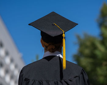 Young woman wearing graduation gown standing against sky