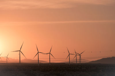 Wind turbines on land against sky during sunset