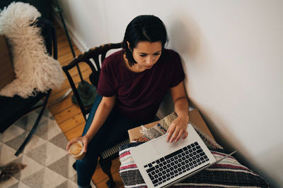 High angle view of woman having tea while using laptop by wall