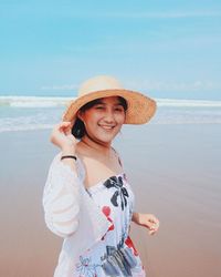 Portrait of smiling young woman standing at beach against sky