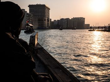 Rear view of man on boat in city at sunset