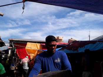 Man sitting at market against sky