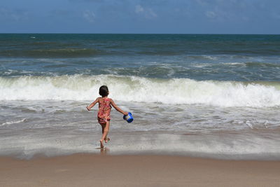 Rear view of girl at beach against sky