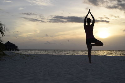 Rear view of woman practicing yoga at beach during sunset