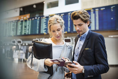 Business people using smart phone while looking at passport in airport