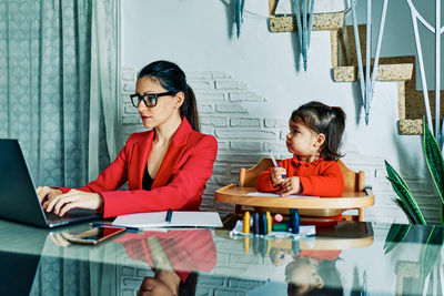 Young executive woman working from home while taking care of her young daughter