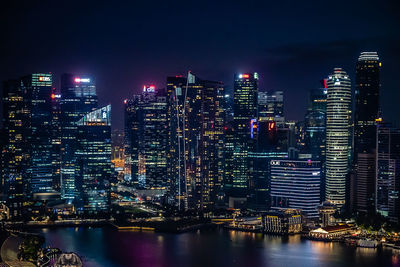 Illuminated modern buildings in city against sky at night