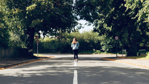 Rear view of girl standing on road against trees