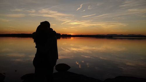 Silhouette couple standing by lake against sky during sunset