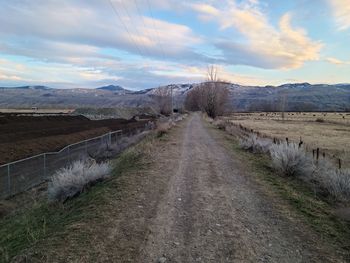 Dirt road amidst landscape against sky