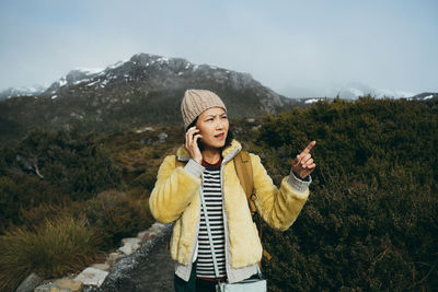 Woman talking over smart phone while standing on mountain against sky