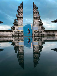 Reflection of woman and temple on lake against sky