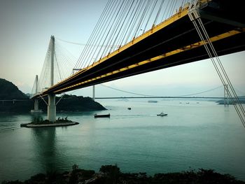 Suspension bridge over river against sky in city