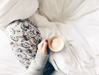 High angle view of woman holding coffee cup on bed