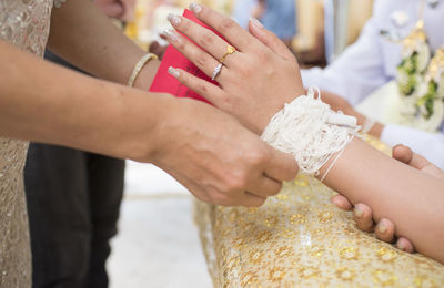 Midsection of woman tying thread on bride during wedding ceremony