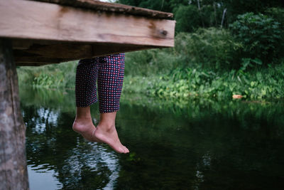 Low section of woman sitting on pier over lake