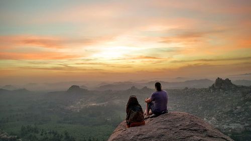 People sitting on rock against sky during sunset