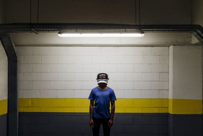 Young man wearing astronaut helmet standing in front of wall at underground walkway