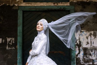 Portrait of woman wearing wedding dress against wall