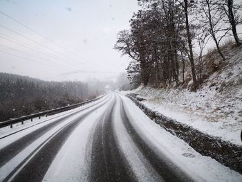 Road amidst trees against sky during winter