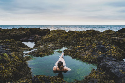 Man on rock by sea against sky