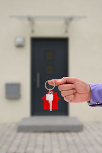 Cropped hand of man holding key ring against house