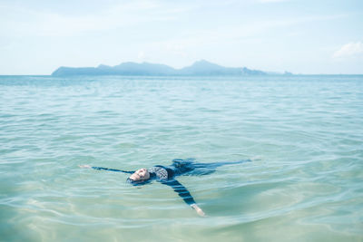 Girl floating on water while swimming in sea against sky