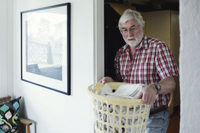 Senior man holding laundry basket while walking through doorway at home