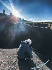 People sitting on mountain against sky on sunny day