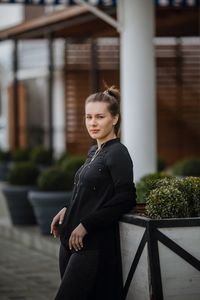 Portrait of young woman standing by potted plant on footpath