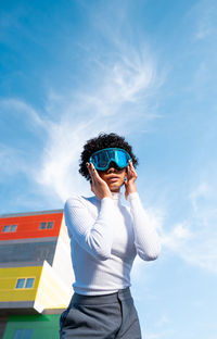 A cool young african american lady with curly hair and ski goggles in an area of modern buildings