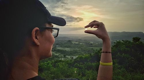 Portrait of man holding sunglasses against sky during sunset