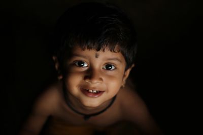 High angle portrait of cute smiling boy against black background