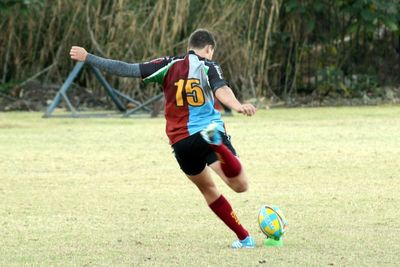 Player kicking rugby ball on playing field