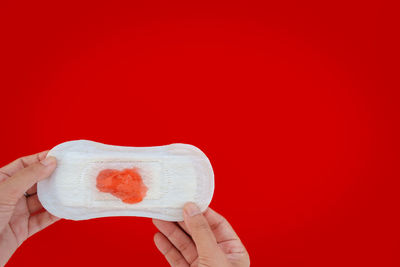 Close-up of hand holding heart shape over red background