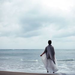 Rear view of woman standing at sea shore against sky