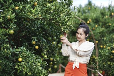 Side view of young woman standing against tree