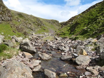 Stream flowing through rocks in valley against sky
