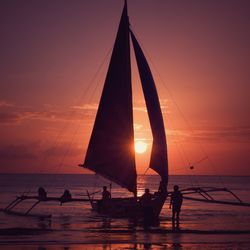 Silhouette people on sailboat by sea against sky during sunset