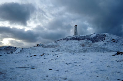 Lighthouse by mountain against sky