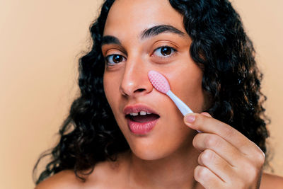 Close-up of young woman applying make-up against pink background