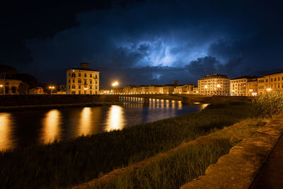 Illuminated buildings by river against sky at night