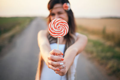 Close-up of woman holding red lollipop while standing on road